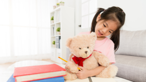 Image of a girl with her teddy doing schoolwork