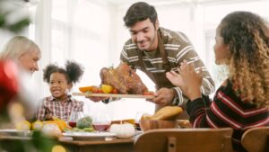 Family celebrating Thanksgiving, sitting around the table and serving turkey