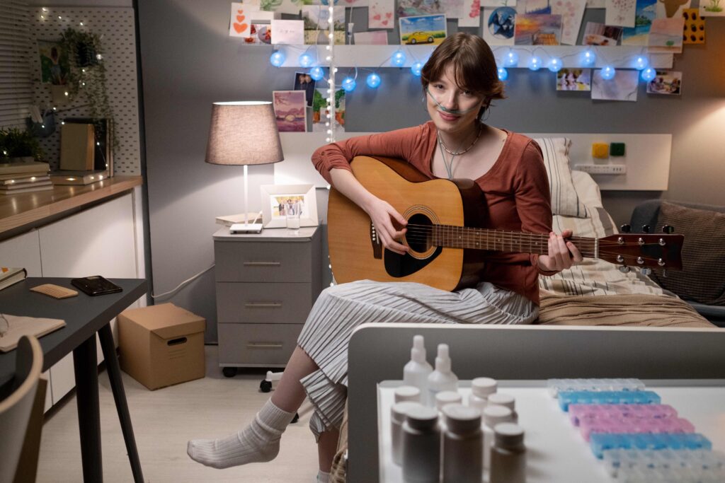 Portrait of sick woman looking at camera while sitting on the bed and playing guitar during her musical therapy at hospital