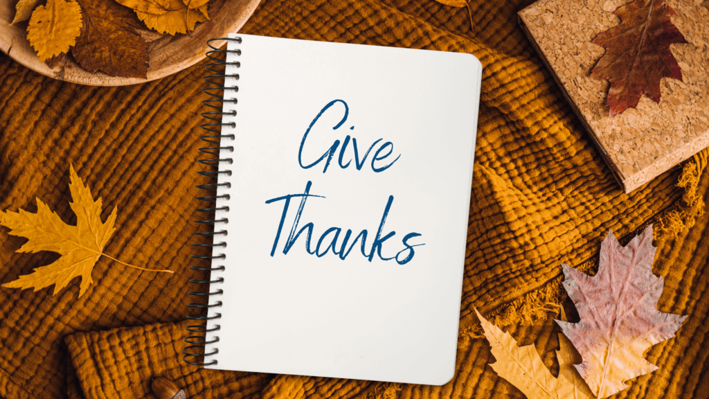 Spiral notebook on a fall blanket with the words Give Thanks, representing Believe in Me’s Thanksgiving Gratitude Wall for grantees.