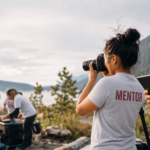 Adult Cougs 4 Kids mentors in white and heather-gray C4K shirts photograph an outdoor event.