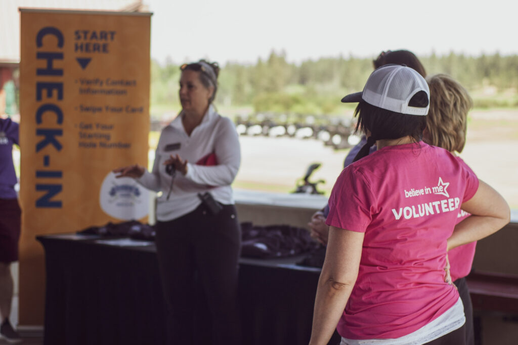 Volunteer welcoming golfers at a past Believe in Me charity golf tournament at Circling Raven