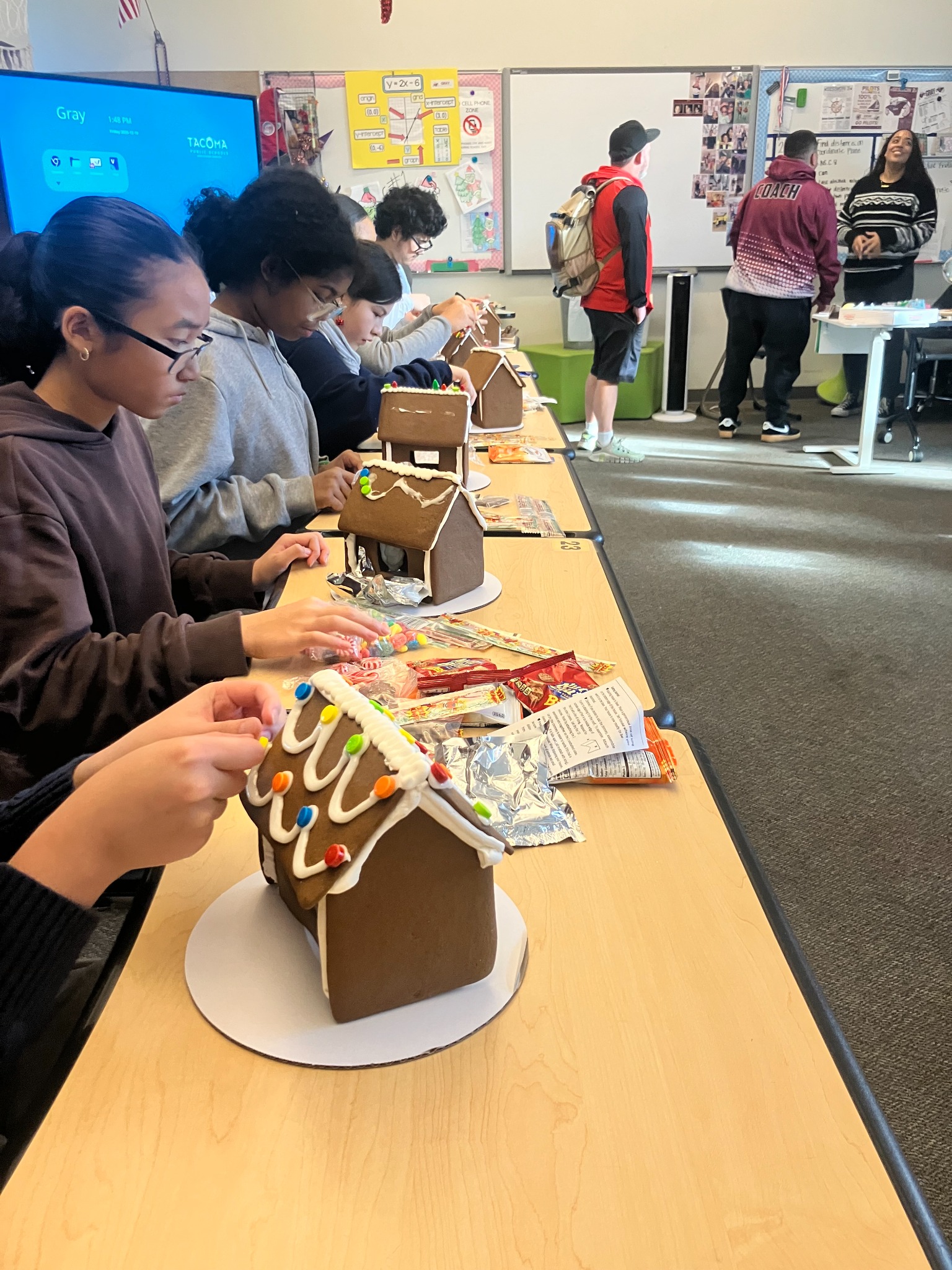 Participants assemble and decorate gingerbread houses along a shared activity table.